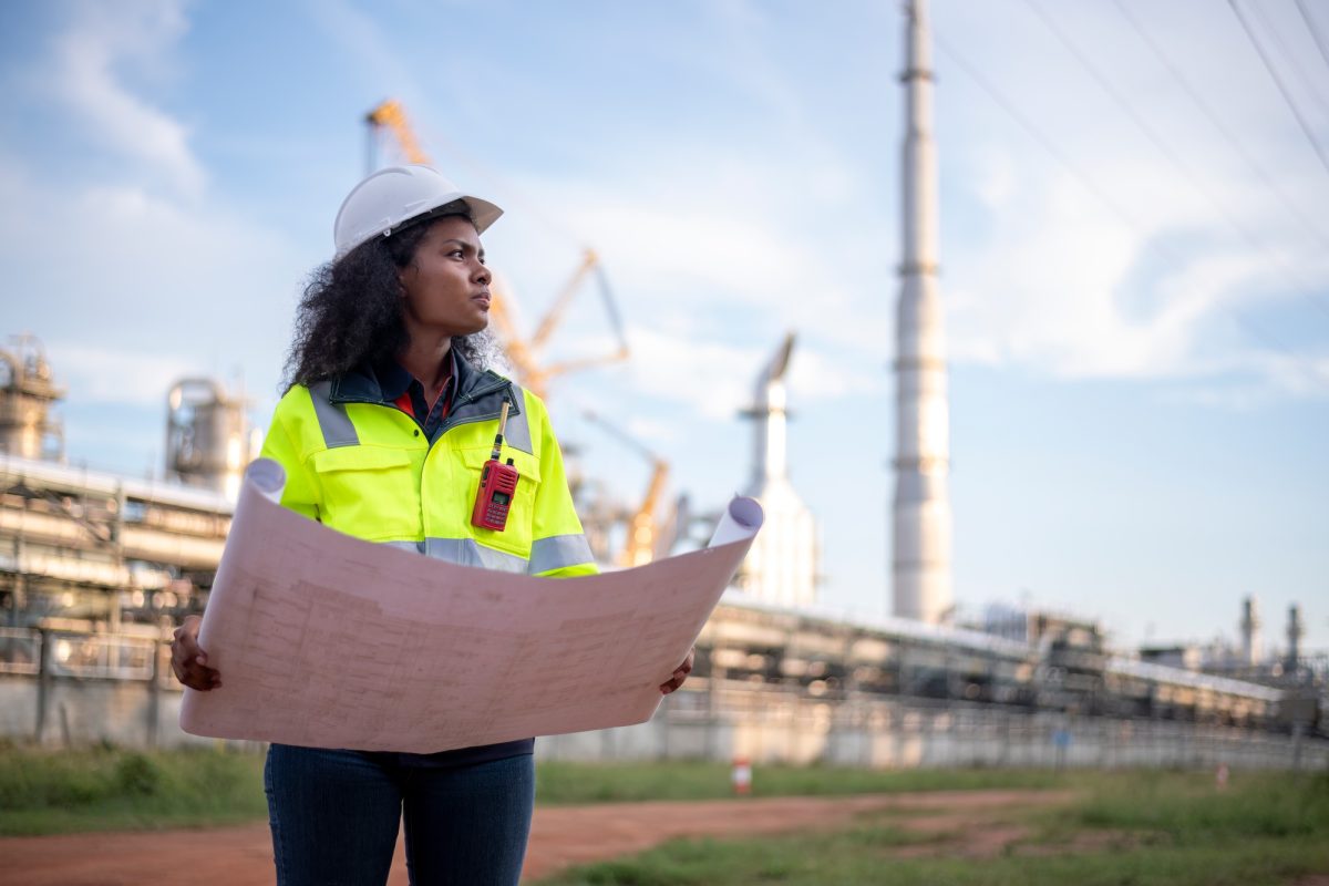 Engineers wearing safety gear, including hard hats examining survey a large blueprint tablet standin